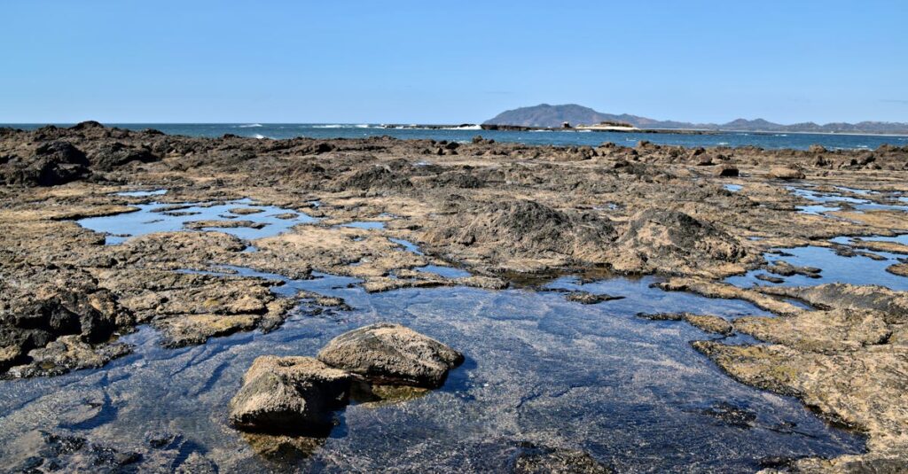 Explore the serene rocky coastline of Tamarindo Beach, Costa Rica under clear blue skies.